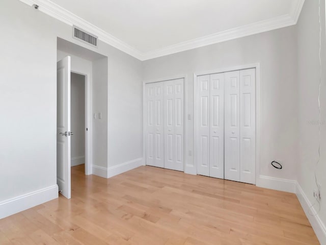 unfurnished bedroom featuring visible vents, multiple closets, ornamental molding, and light wood finished floors