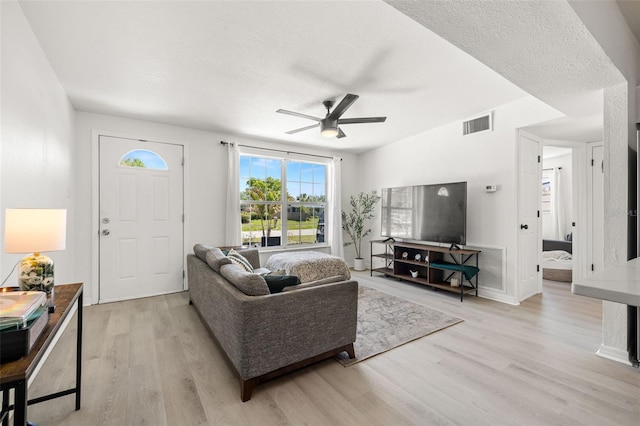 living area featuring a ceiling fan, light wood-style floors, visible vents, and a textured ceiling