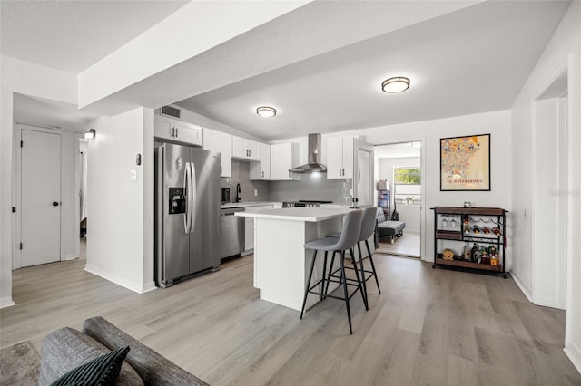 kitchen featuring wall chimney range hood, a breakfast bar, light countertops, decorative backsplash, and appliances with stainless steel finishes