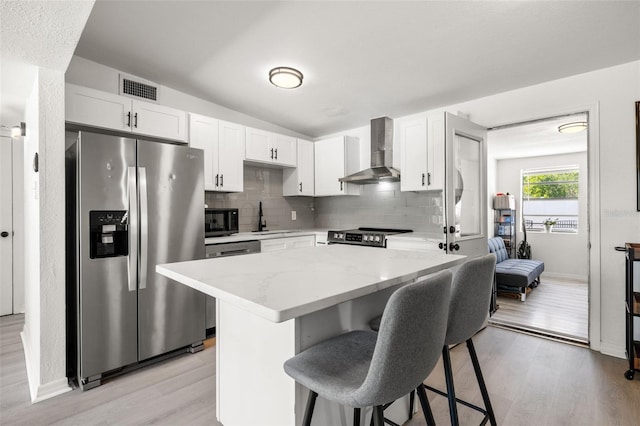 kitchen with visible vents, a kitchen breakfast bar, stainless steel appliances, wall chimney exhaust hood, and a sink