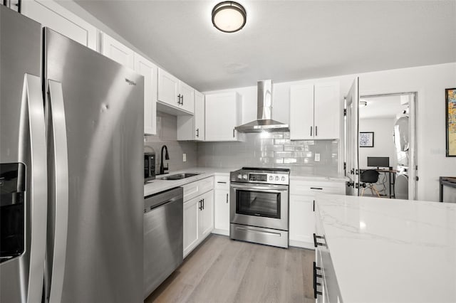 kitchen featuring light stone countertops, a sink, stainless steel appliances, wall chimney exhaust hood, and tasteful backsplash