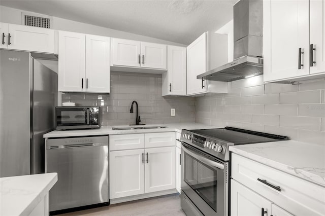 kitchen featuring visible vents, appliances with stainless steel finishes, white cabinets, wall chimney exhaust hood, and a sink