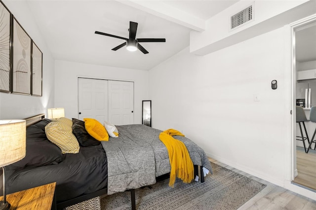 bedroom with visible vents, ceiling fan, beam ceiling, wood finished floors, and a closet