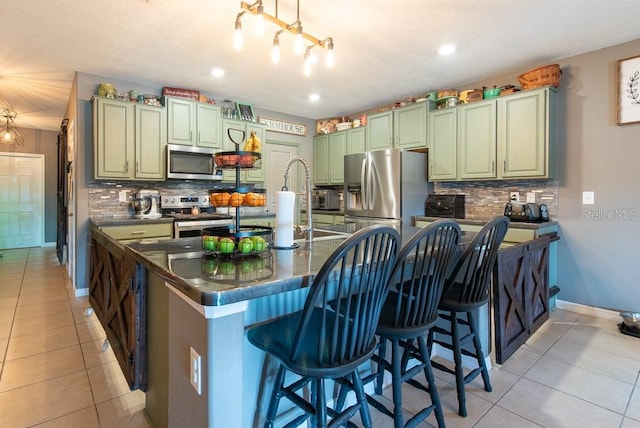 kitchen with green cabinetry, light tile patterned flooring, stainless steel appliances, decorative backsplash, and dark countertops