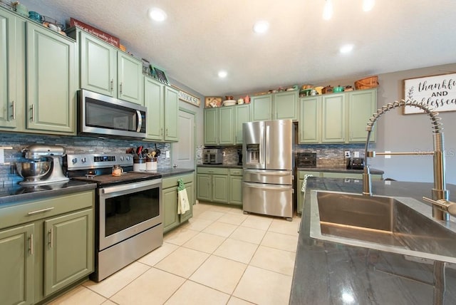 kitchen with dark countertops, green cabinetry, light tile patterned floors, appliances with stainless steel finishes, and a sink