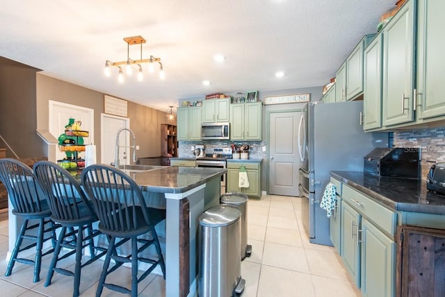 kitchen with dark countertops, a sink, light tile patterned flooring, stainless steel appliances, and green cabinetry