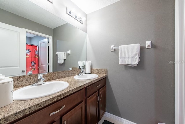 full bath with double vanity, baseboards, and a sink