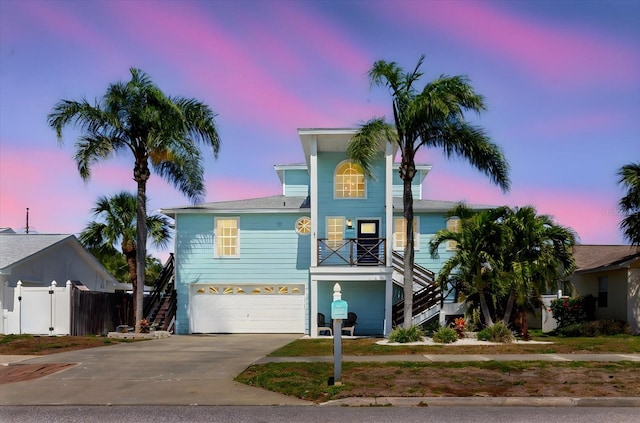 coastal home with stairway, an attached garage, fence, and driveway