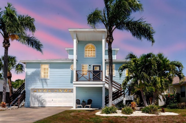 coastal home with a garage, concrete driveway, and stairs