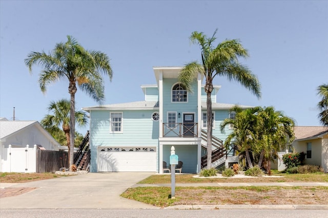 coastal home with concrete driveway, stairs, a garage, and fence