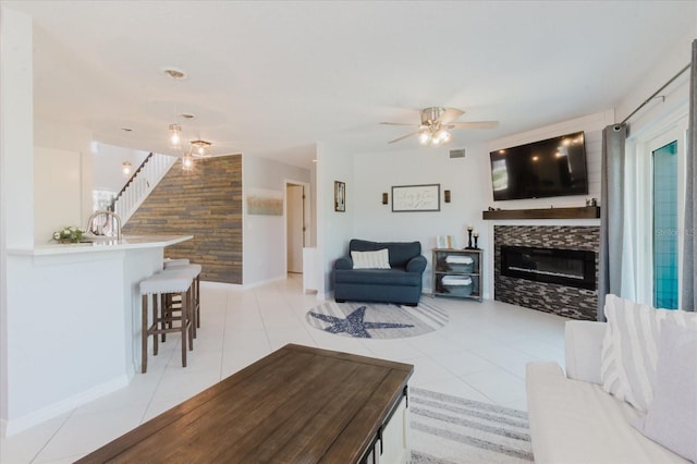 living area featuring visible vents, an accent wall, ceiling fan, a fireplace, and light tile patterned flooring