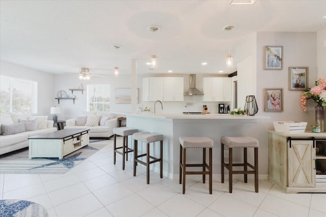 kitchen with a healthy amount of sunlight, a kitchen breakfast bar, a peninsula, and wall chimney range hood