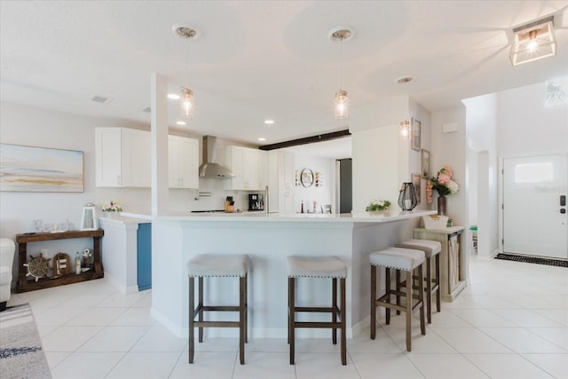 kitchen featuring a kitchen breakfast bar, white cabinetry, and wall chimney range hood