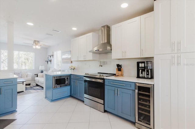 kitchen with light countertops, wine cooler, appliances with stainless steel finishes, wall chimney exhaust hood, and open floor plan