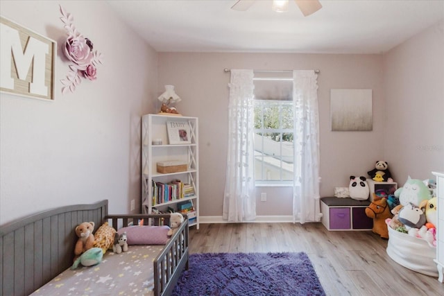 bedroom with a crib, a ceiling fan, baseboards, and wood finished floors