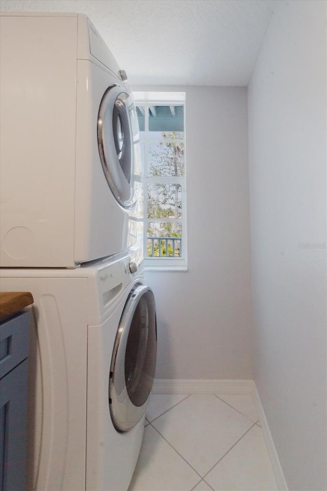 washroom featuring baseboards, laundry area, stacked washer and dryer, a textured ceiling, and tile patterned floors