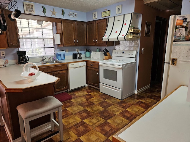 kitchen featuring light countertops, range hood, white appliances, a textured ceiling, and a sink