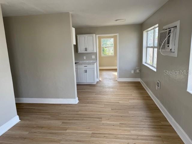 unfurnished dining area featuring light wood-type flooring, baseboards, and a wall unit AC