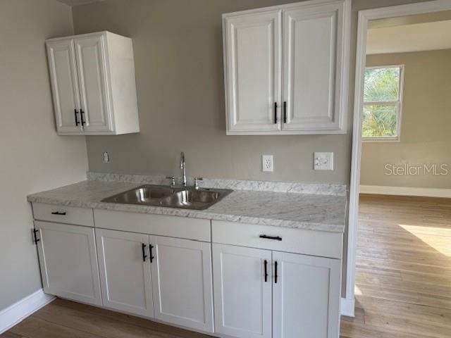 kitchen featuring white cabinetry, light wood-style flooring, baseboards, and a sink