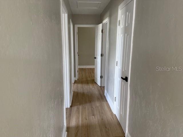 corridor with baseboards, attic access, a textured wall, and wood finished floors