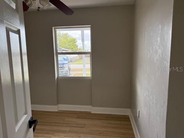 empty room featuring light wood finished floors, a ceiling fan, and baseboards