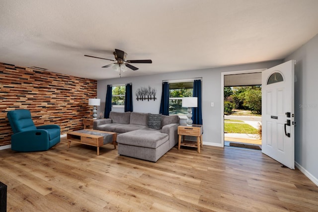 living room with ceiling fan, a textured ceiling, light wood-type flooring, and baseboards