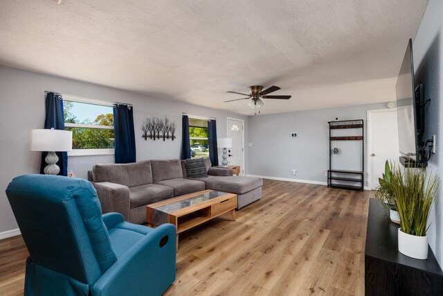 living room with ceiling fan, light wood-style flooring, baseboards, and a textured ceiling