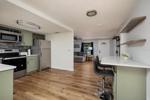 kitchen with green cabinets, open shelves, light countertops, and appliances with stainless steel finishes