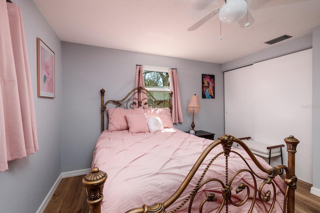 bedroom with visible vents, a ceiling fan, a textured ceiling, wood finished floors, and baseboards