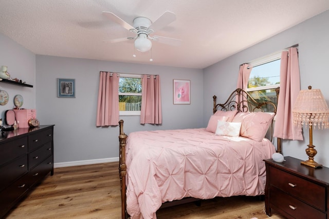 bedroom with multiple windows, a textured ceiling, light wood-style flooring, and baseboards