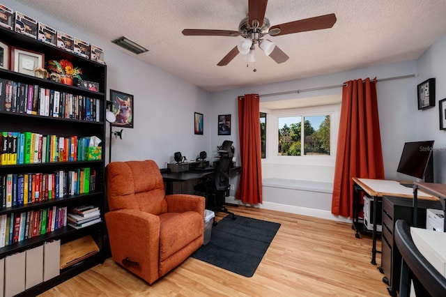 living area with a ceiling fan, baseboards, wood finished floors, visible vents, and a textured ceiling