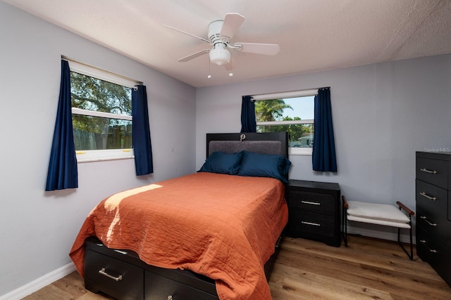 bedroom with multiple windows, wood finished floors, baseboards, and ceiling fan