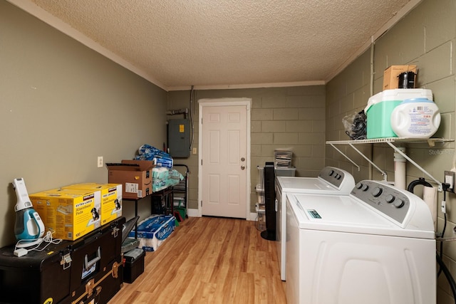 washroom featuring concrete block wall, light wood finished floors, laundry area, electric panel, and washing machine and dryer