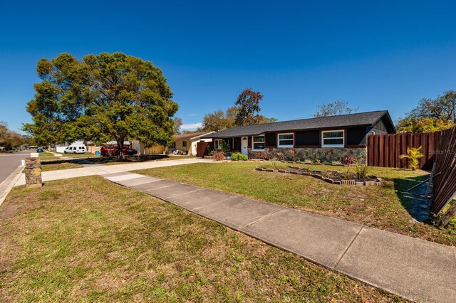 ranch-style house featuring a front lawn, fence, stone siding, and driveway