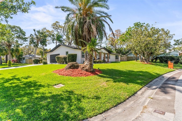 view of front facade featuring a front lawn, fence, stucco siding, a garage, and driveway