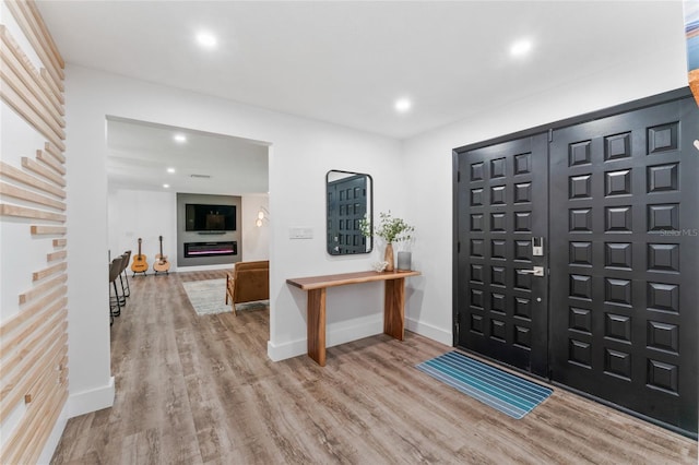 entryway with a glass covered fireplace, recessed lighting, wood finished floors, and baseboards