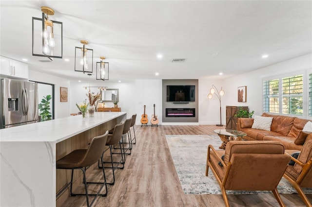 living area with visible vents, baseboards, recessed lighting, light wood-style floors, and a glass covered fireplace