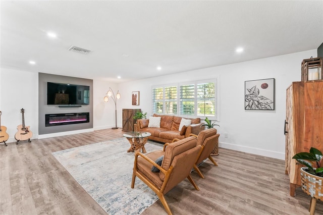 living area featuring recessed lighting, visible vents, light wood-style floors, and a glass covered fireplace