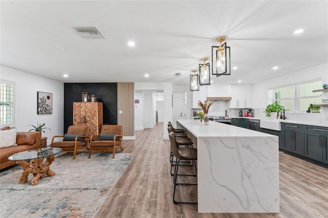 kitchen with visible vents, light stone countertops, open floor plan, a breakfast bar area, and light wood-type flooring