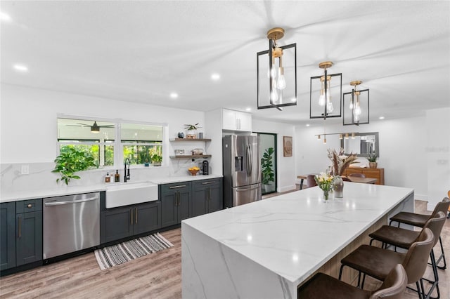 kitchen featuring a sink, light stone counters, appliances with stainless steel finishes, a kitchen breakfast bar, and open shelves