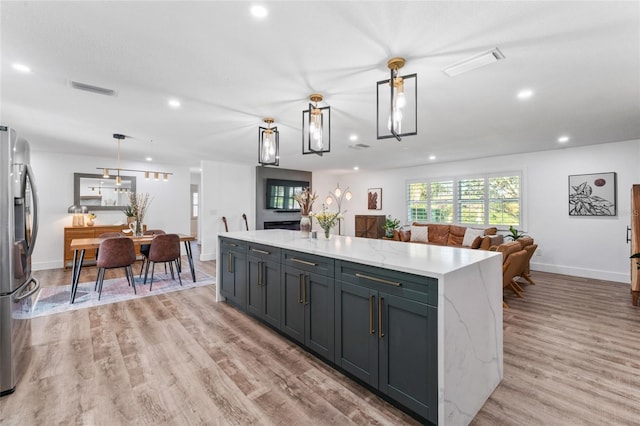 kitchen featuring visible vents, a kitchen island, light wood-style flooring, stainless steel fridge with ice dispenser, and pendant lighting