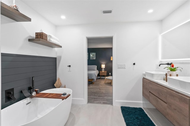 ensuite bathroom with visible vents, double vanity, a freestanding bath, a sink, and tile patterned floors