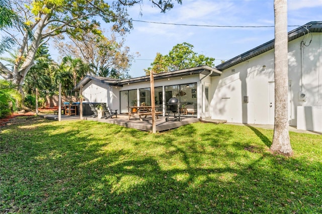 rear view of house featuring stucco siding, a wooden deck, and a yard