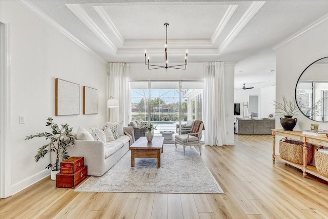 living room with wood finished floors, an inviting chandelier, ornamental molding, a textured ceiling, and a raised ceiling