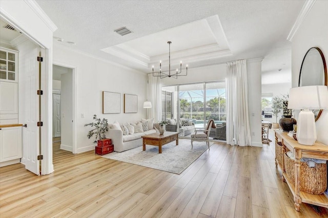 living room with a tray ceiling, visible vents, light wood finished floors, and ornamental molding