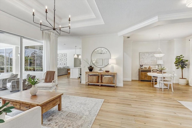 living room with baseboards, crown molding, light wood-type flooring, a raised ceiling, and a chandelier