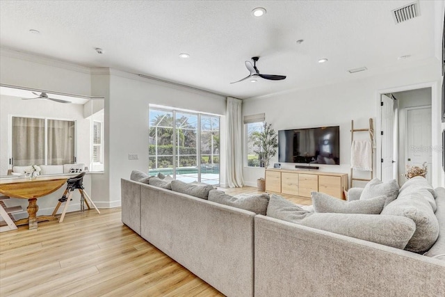 living area with light wood finished floors, visible vents, a textured ceiling, and a ceiling fan