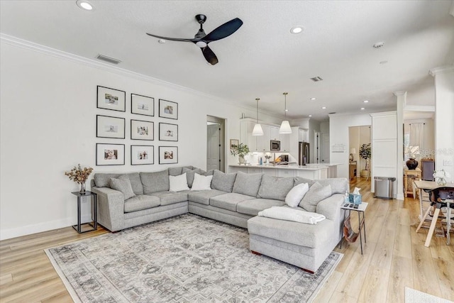 living room with ceiling fan, visible vents, ornamental molding, and light wood finished floors