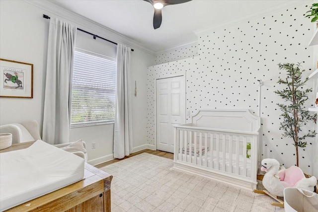 bedroom with a ceiling fan, baseboards, wallpapered walls, a nursery area, and crown molding