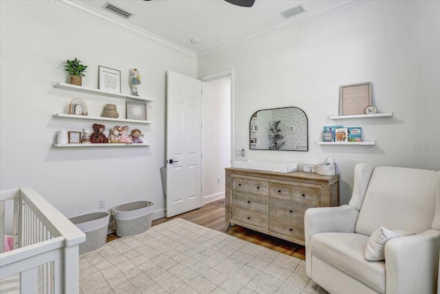 bedroom with visible vents, a nursery area, wood finished floors, and crown molding